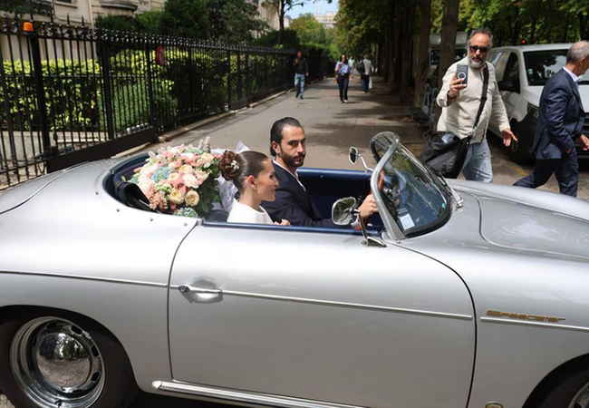 Thylane Blondeau ve eşi Benjamin Attal, gümüş rengi bir Porsche 356 Speedster ile ortak geleceklerine doğru hızla ilerliyor. Gelin, saçını zarif beyaz çiçeklerle süslenmiş şık bir topuz şeklinde kullanmış..